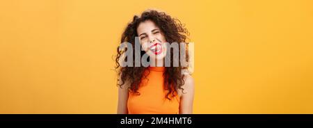 Portrait d'une jeune fille caucasienne à l'allure entraînante et élégante, avec des cheveux bouclés et un rouge à lèvres, montrant la langue avec une inclinaison d'expression chaude rebelle Banque D'Images