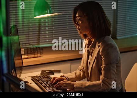 Jeune femme se concentrant sur son travail en ligne sur l'ordinateur, elle tapant des codes sur le clavier travaillant au bureau jusqu'à tard la nuit Banque D'Images