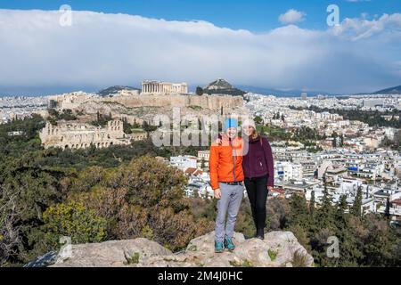 Couple, touristes se tenant sur des rochers, vue de la colline de Philopapos sur la ville, panorama du Temple du Parthénon et de l'Amphithéâtre d'Hérode, Acropole Banque D'Images