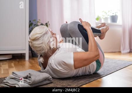 Femme allongé sur un tapis de yoga faisant apanasana. Une femme qui se détend au sol à la maison. Banque D'Images