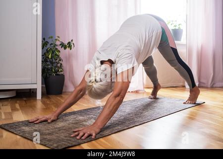 Femme âgée faisant de l'exercice de yoga dans la salle face à la posture du chien Banque D'Images
