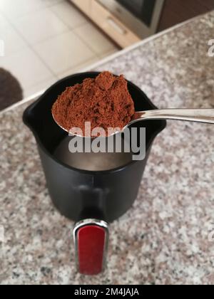 gros plan une cuillère de café turc moulu se préparant à faire du café dans une machine à café turque vue de dessus sur le comptoir de cuisine en marbre et p flou Banque D'Images