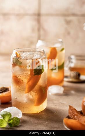 Deux verres de cocktail d'abricot, fizz, thé glacé à la menthe fraîche. Fond rose beige. Orientation verticale Banque D'Images