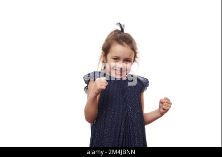 Portrait émotionnel méchant petite fille enfant dans une belle robe bleue élégante, des poings et souriant à l'appareil photo Banque D'Images