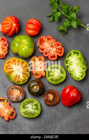 Moitiés de tomates rouges et vertes sur la table. Branche de persil. Pose à plat. Arrière-plan gris. Banque D'Images