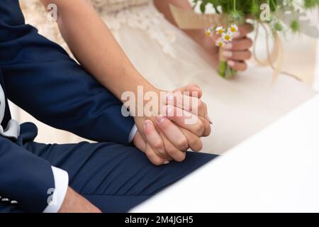 mariée et marié tenant les mains, assis devant l'autel. Gros plan des mains secouant et tenant le bouquet Banque D'Images