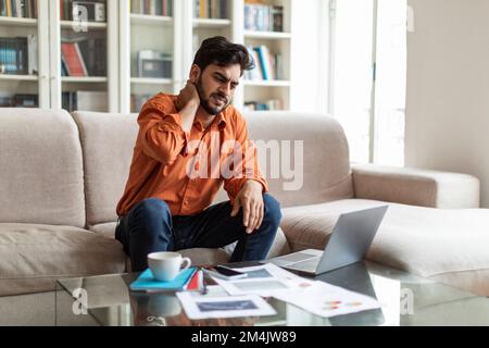 Fatigué stressé homme arabe ayant des douleurs au cou, travaillant de la maison Banque D'Images