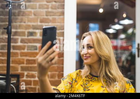 femme blonde de belle apparence satisfaite prenant un selfie après la procédure de cheveux au salon, moyenne gros plan. Photo de haute qualité Banque D'Images