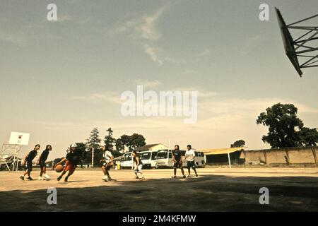 Les adolescents jouant au basket-ball sur un terrain de basket-ball qui a parfois aussi servi de parking pour les bus transportant des touristes religieux qui veulent visiter la région de Daarut Tauhiid à Gegerkalong, Bandung, West Java, Indonésie. Banque D'Images