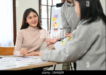 Un groupe de graphistes asiatiques du millénaire se réunit pour discuter et planifier le schéma de couleurs pour une nouvelle conception d'interface d'application mobile. Banque D'Images