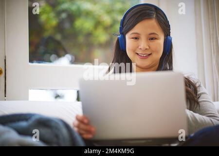 En train de regarder tous ses programmes préférés. une jeune femme attrayante portant un casque tout en utilisant un ordinateur portable à la maison. Banque D'Images