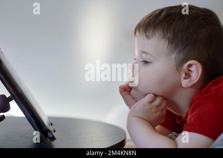 beau garçon regardant des dessins animés sur une tablette de table Banque D'Images