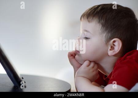 beau garçon regardant des dessins animés sur une tablette de table Banque D'Images