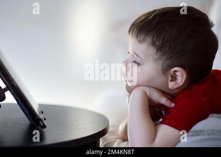 beau garçon regardant des dessins animés sur une tablette de table Banque D'Images