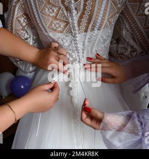 Le dos de la mariée, vêtu d'une robe de mariage, les filles aident les épouses à porter une robe. Banque D'Images