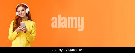 La technologie, le shopping et les gens concept. Hipster mignon moderne redhead girl wearing white casque, holding smartphone, souriant insouciant, profiter d'une belle Banque D'Images