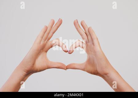 Montrez votre amour. Photo en studio d'une personne méconnaissable mains faisant une forme de coeur sur un fond gris. Banque D'Images