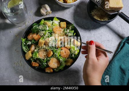 Gros plan de la femme mangeant de la salade César à la fourchette sur une table en marbre gris Banque D'Images