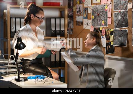 Les agents féminins chargés de l'application de la loi dévoilantes l'identité d'un criminel terroriste lorsqu'ils travaillent au bureau la nuit. Copier l'espace Banque D'Images