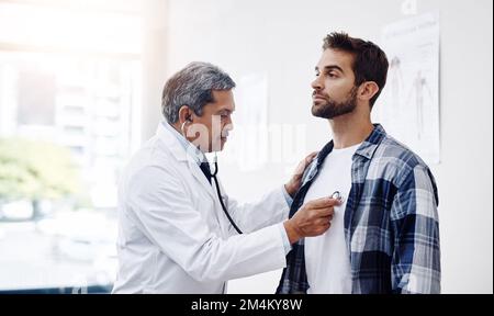 Prenez une profonde respiration... un homme mature médecin et patient ayant une discussion dans le bureau des médecins pendant un examen. Banque D'Images