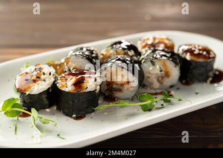 Petits pains Maki à l'anguille, aux graines de sésame et à la sauce soya sur une assiette blanche. délicieux plats japonais avec un rouleau de sushis. Banque D'Images
