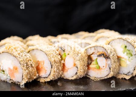 Roulés de sushi frits à chaud avec crevettes, saumon, concombre et fromage philadelphia isolé sur fond noir. Concept de menu sushi. Cuisine japonaise. Gros plan Banque D'Images