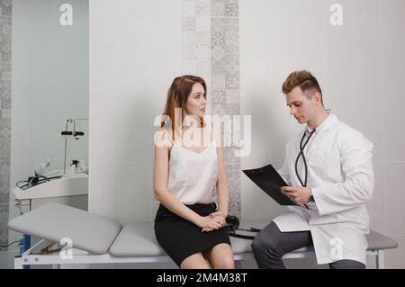 un médecin de sexe masculin communique avec un patient en enregistrant les relevés tout en étant assis sur un canapé dans le bureau Banque D'Images