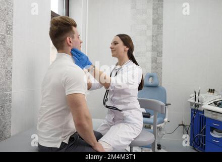 une jeune femme médecin examine les ganglions lymphatiques d'un patient masculin dans une clinique moderne. Banque D'Images