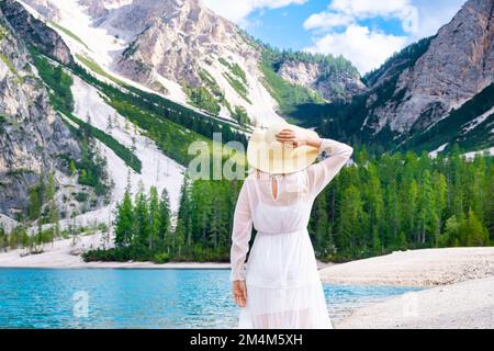 Vue arrière de la femme en robe blanche et chapeau sur la rive du lac Braies contre les montagnes. Concept de vacances et de voyages. Banque D'Images