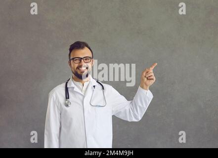 Un jeune homme heureux médecin dans un manteau de laboratoire pointe son doigt sur le côté avec l'espace de copie Banque D'Images