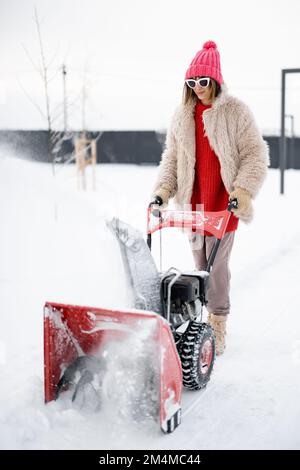 Une femme enlève la neige de la voie avec une fraise à neige Banque D'Images