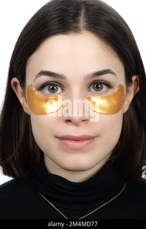 Sous la zone de la peau des yeux. Gros plan du visage de la jeune femme avec un coussin de masque de collagène hydratant sur une peau du visage fraîche et saine sur fond blanc. Banque D'Images