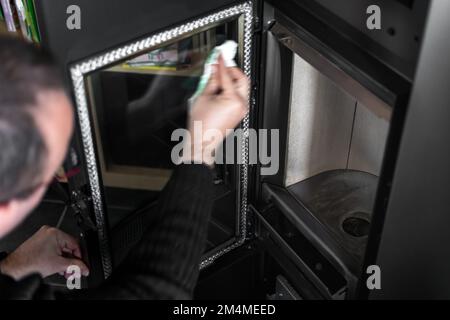 Homme nettoyant la cendre sur le verre d'une pastille ou d'un poêle à bois avec une serviette en papier et de l'eau chaude Banque D'Images