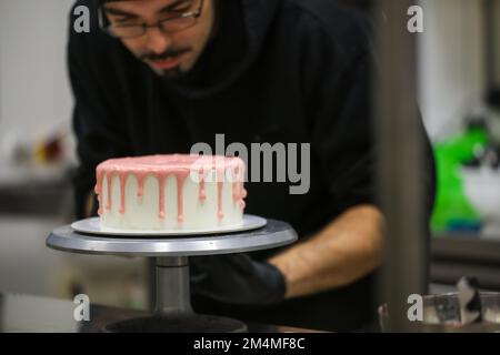 chef cuisinier de gâteau préparant un goutter rose sur un gâteau blanc dépoli pour la fête d'anniversaire de petite fille au laboratoire de cuisine Banque D'Images