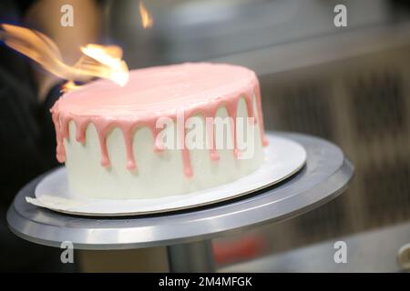 chef cuisinier de gâteau préparant un goutter rose sur un gâteau blanc dépoli pour la fête d'anniversaire de petite fille au laboratoire de cuisine Banque D'Images