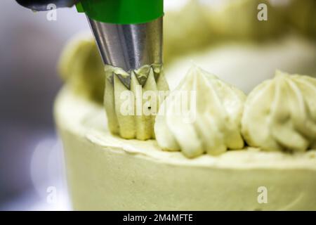 chef pâtissier créateur de tourbillons avec sac de passepoil crème pistache sur un gâteau au chocolat vert givré en couches Banque D'Images
