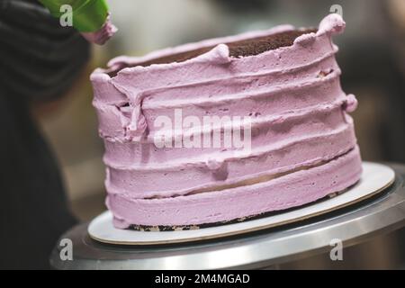 chef cuisinier à gâteau utilisant la crème de rose comblant sac de tuyauterie décorant le gâteau au chocolat noir superposé au laboratoire de cuisine Banque D'Images