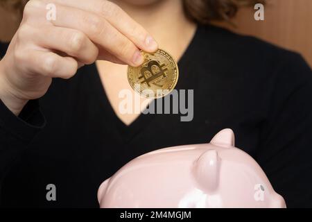 La main de femme tient et met l'argent virtuel de la pièce de bitcoin d'or à la boîte de banque de piggy rose . Concept de crypto-monnaie et d'épargne Banque D'Images