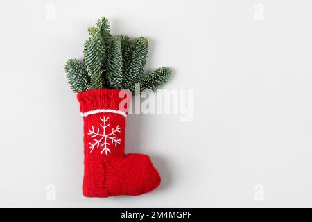 Chaussette de Noël rouge avec un flocon de neige blanc brodé et des branches vertes d'un sapin de Noël sur fond gris avec un emplacement pour le texte. Banque D'Images