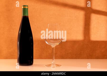 Verre de vin rouge avec une bouteille de vin sans étiquette avec lumière du soleil à travers une fenêtre. Banque D'Images