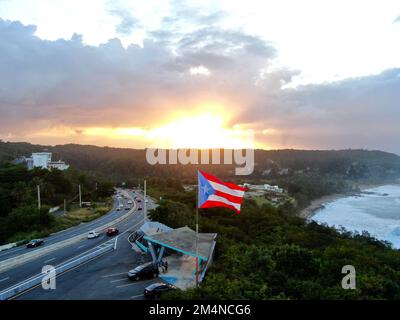 Un gros plan aérien du drapeau de Porto Rico qui agite dans les airs près d'une autoroute au coucher du soleil Banque D'Images