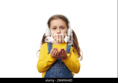 Charmante fille de 5-6 ans, avec deux queues de cheval, soufflant un baiser d'air, regardant la caméra, isolée sur blanc Banque D'Images