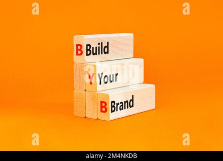 BYB construisez votre symbole de marque. Mots-clés BYB construisez votre marque sur des blocs de bois sur une belle table orange fond orange. Business et BYB Build Banque D'Images