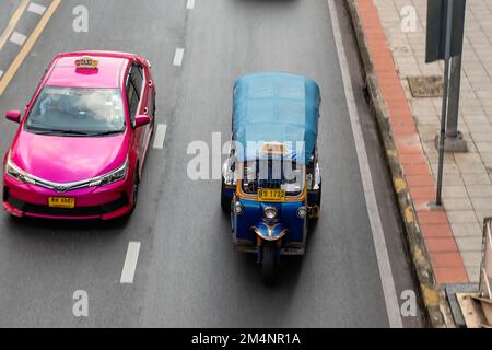 Bangkok, Thaïlande. 16 novembre 2022. Tuk tuk en voiture à côté d'un taxi rose sur une route dans le centre-ville de Bangkok Banque D'Images