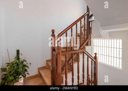 Escalier spacieux avec marches en marbre et rambardes en bois menant à l'étage supérieur sur fond de murs blancs. Lumière du jour depuis le puits de la fenêtre Banque D'Images