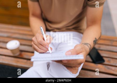 Prise de vue courte en grand angle d'un élégant artiste masculin avec des mains tatouées sur un banc et des croquis avec stylo sur papier. Banque D'Images