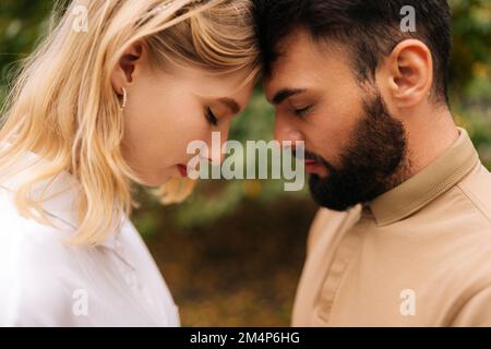 Gros plan de couple marié aimant debout avant touché avec les yeux fermés. Joyeux jeune homme barbu et jolie femme blonde à la date romantique à l'intérieur Banque D'Images