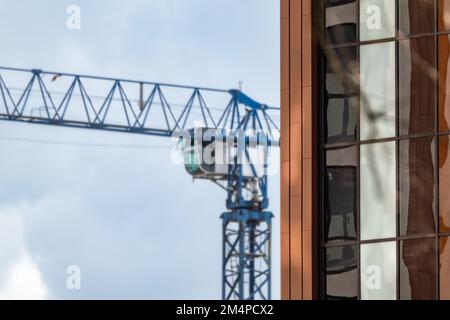 Bâtiment moderne avec façade en verre réfléchissant marron et blanc et grande grue bleue en arrière-plan Banque D'Images