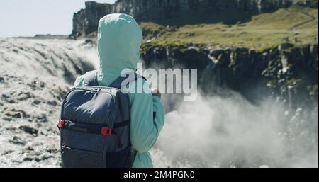 Vue arrière d'une femme se tenant au bord de la falaise et regardant la cascade de Detifoss en Islande Banque D'Images