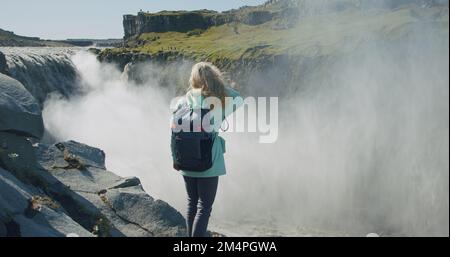 Femme debout au bord de la falaise et regardant la cascade de Detifoss en Islande Banque D'Images